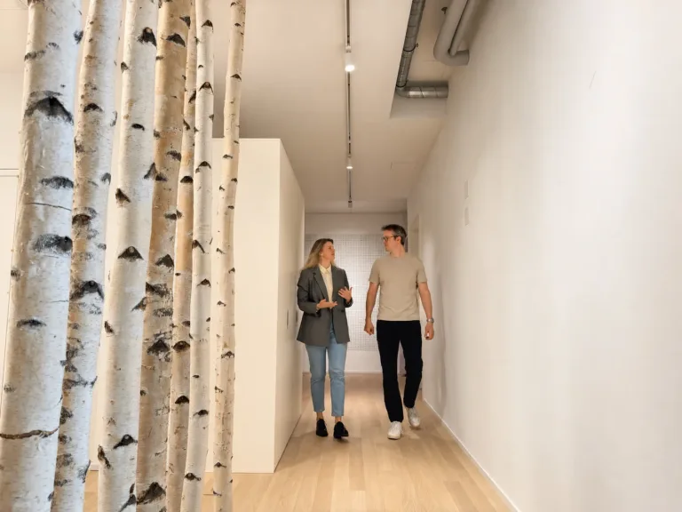 Barbara und Mitgründer Martin Schuck gehen im Gespräch durch den hellen Flur der klaro ADHS Praxis in Zürich, links Birkenstämme